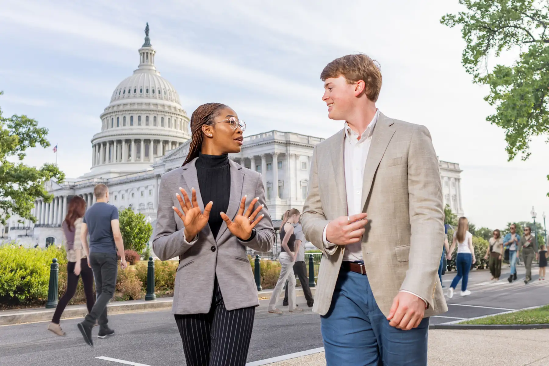 Two students in suits walk and talk with the U.S. Capitol building in the background.